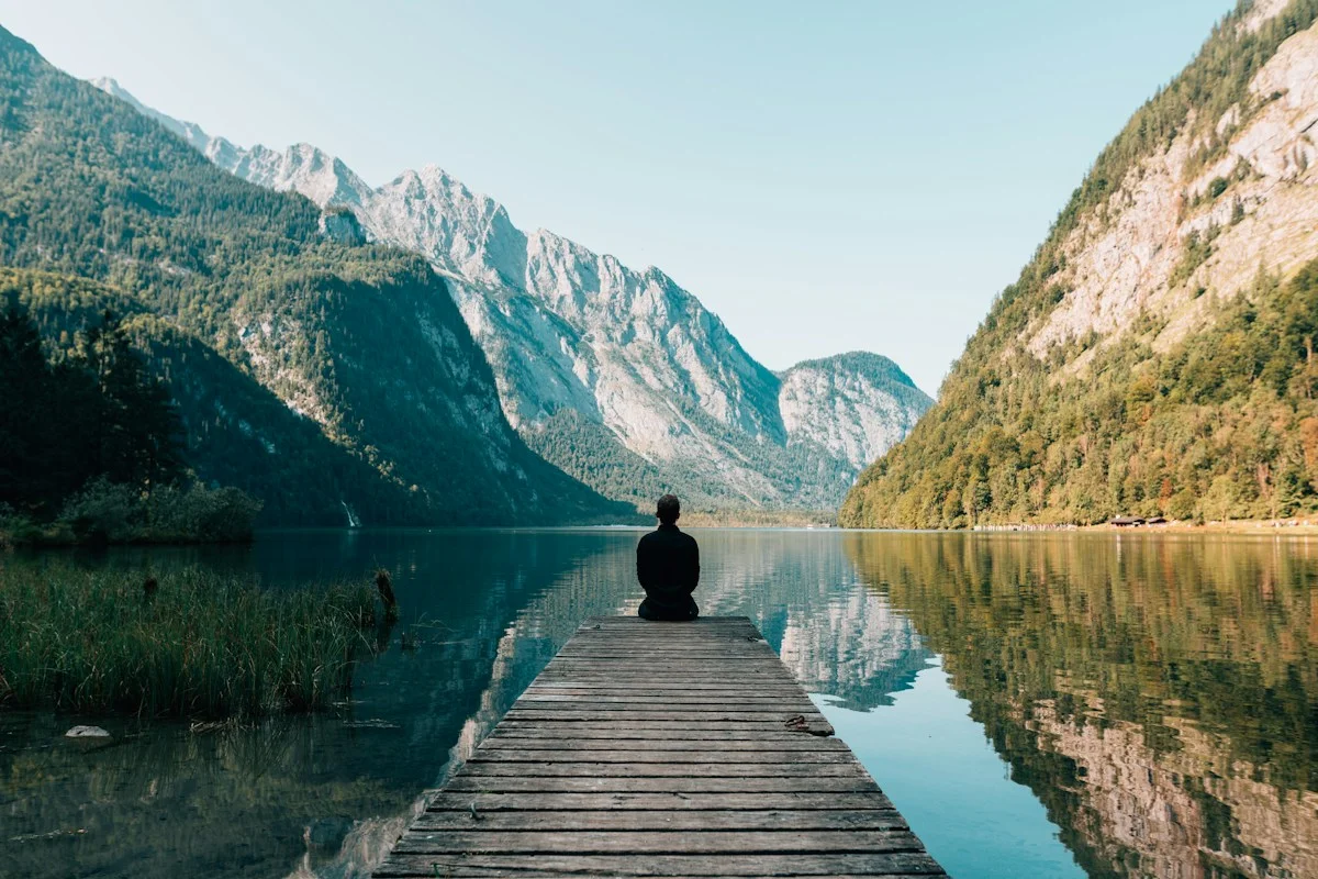 Persoană singură pe un ponton de lemn, privind spre un lac între munți, moment de reflecție asupra relației